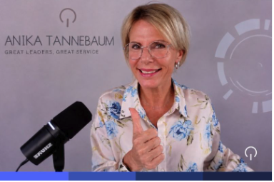 Anika Tannebaum lächelt mit erhobenem Daumen vor einem Mikrofon, im Hintergrund ihr persönliches Branding "Great Leaders, Great Service"